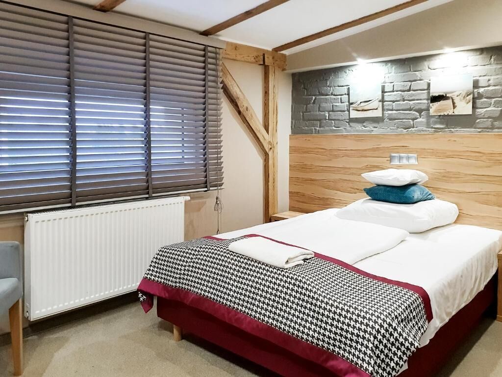 Ein Schlafzimmer mit einem Bett, einem Heizkörper, einem Fenster mit Jalousien und einer Steinwand mit einer Lampe.