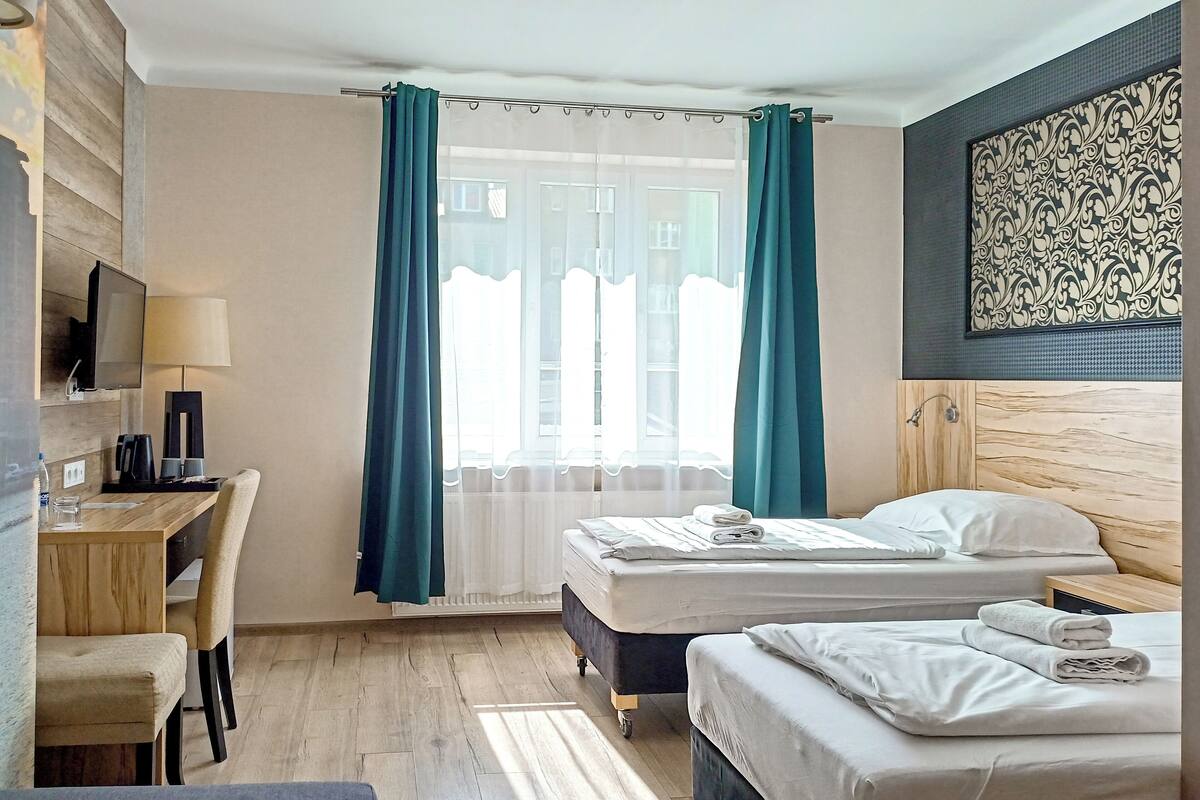 Une chambre d’hôtel avec deux lits, un bureau avec une chaise, une télévision et une fenêtre avec des rideaux.