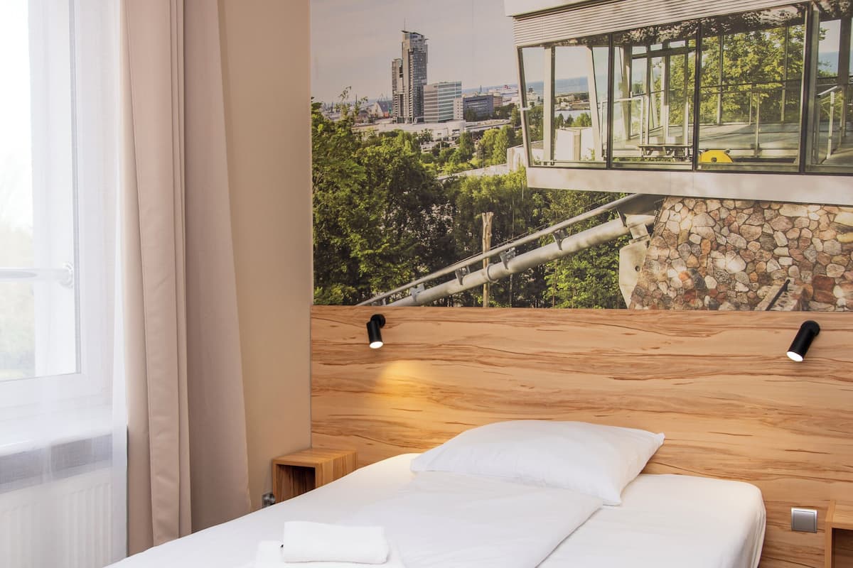 Une chambre d’hôtel moderne avec un lit, une tête de lit en bois et une fresque représentant un paysage urbain sur le mur.