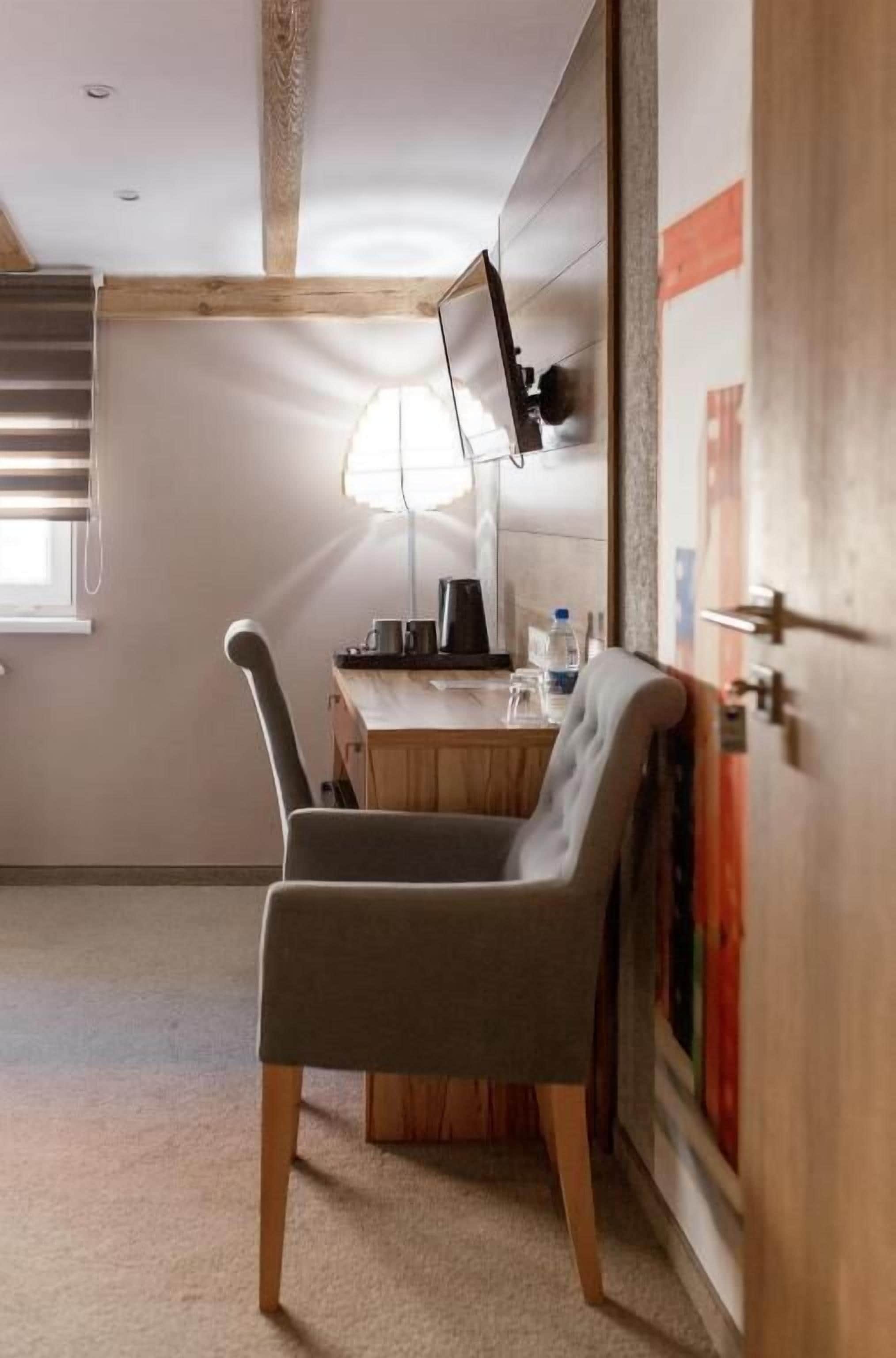 A cozy room with a wooden desk, a chair, a lamp, and a wall-mounted TV.