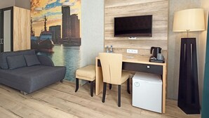 Une chambre d’hôtel moderne équipée d’un canapé, d’un bureau avec une chaise, d’une télévision, d’une lampe et d’un réfrigérateur.
