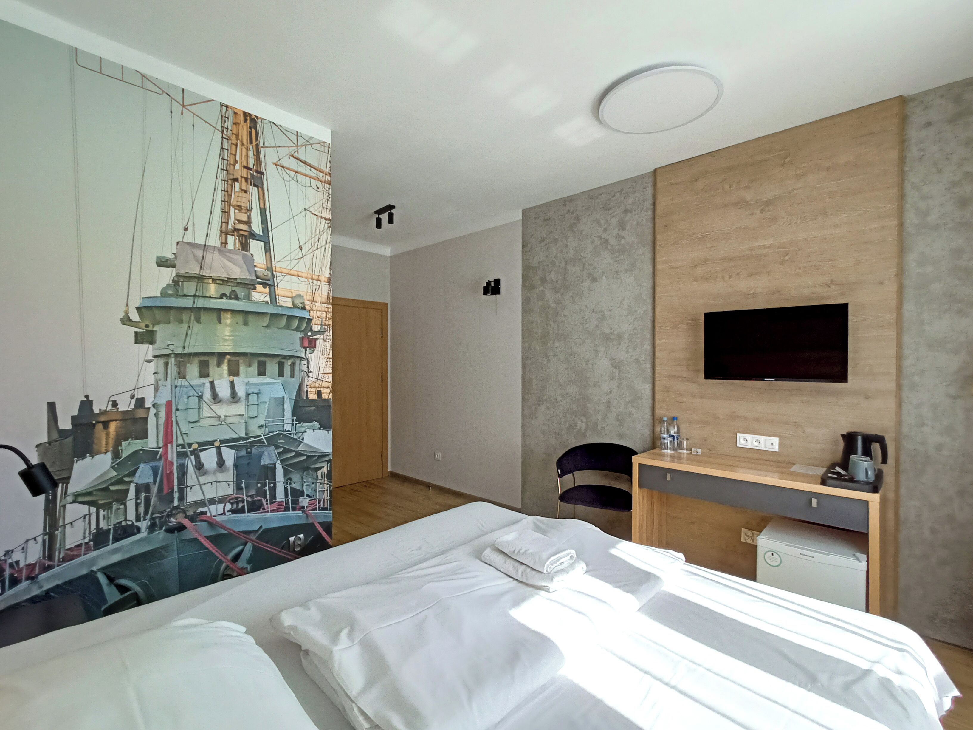 A hotel room with a bed, a desk, a chair, a television, and a large wall mural.