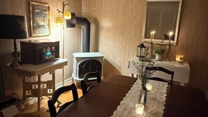 A dining area with a wooden table, chairs, a lace table runner, a fireplace, a mirror, and wall-mounted lamps.