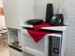 A kitchen with a microwave, a black appliance on top, and a red cloth on the counter.