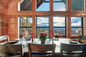 A wooden interior with a dining table set for two, large windows, and a view of the outdoors.