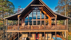 A two-story log cabin with a stone foundation, wooden balconies, and a stone fireplace.