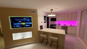 Eine moderne Küche mit Barbereich, integriertem Fernseher und einer rosa beleuchteten Spritzschutzwand.