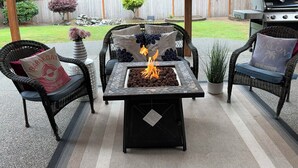 An outdoor patio with a fire feature, wicker furniture, and a view of the backyard. - Modern Self check-inLarge Fenced Yard A/C Close to Everything Quiet Neighborhood (Olympia)