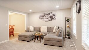 A living room with a sectional sofa, a coffee table, and a wall-mounted clock. - Modern Self check-inLarge Fenced Yard A/C Close to Everything Quiet Neighborhood (Olympia)