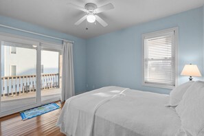 A bedroom with a bed, a ceiling fan, a window with blinds, and a view of a balcony. - Oceanside, Steps to the Beach, Hot Tub, Pet Friendly, Ocean and Sound Views (Frisco)