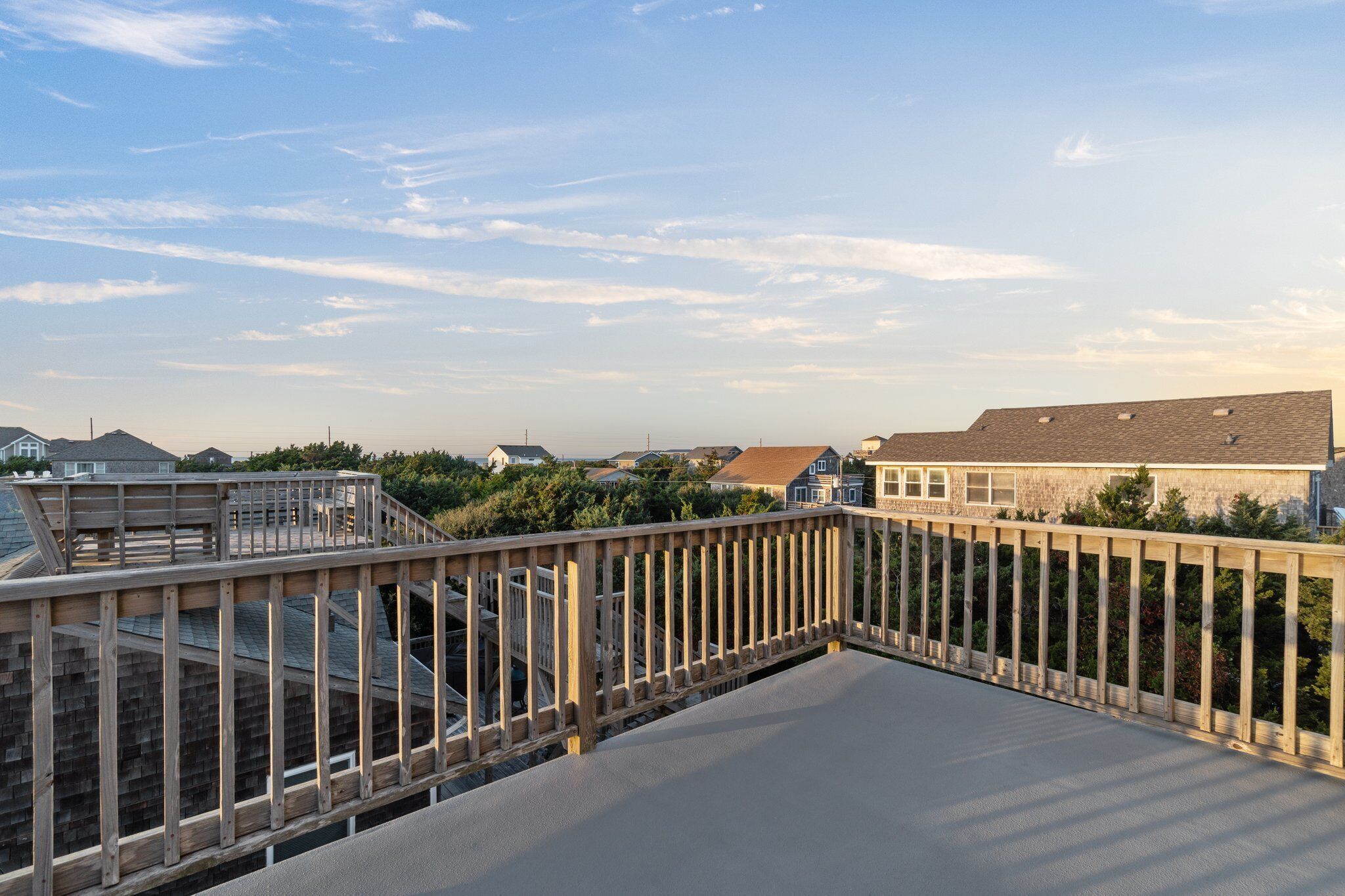A wooden deck with a railing overlooking a residential area with houses and trees.
