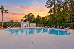 Una piscina con sillas de descanso y un pequeño edificio, rodeado de árboles y un cielo al atardecer.