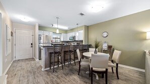A modern kitchen with a central island, bar stools, and a dining table with chairs.
