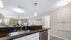 A modern kitchen with a granite countertop, stainless steel sink, and white cabinetry.