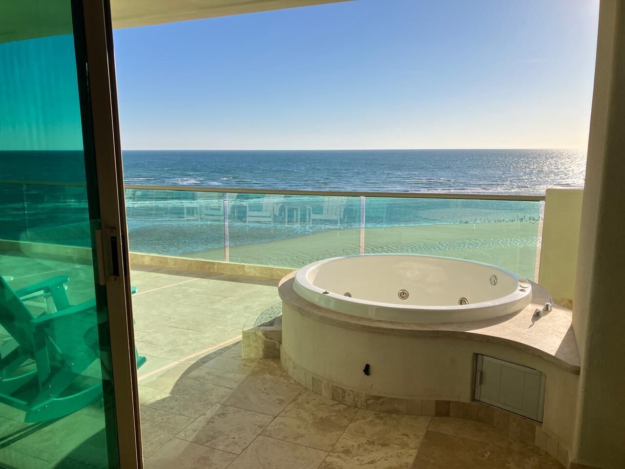 A balcony with a jacuzzi, clear glass doors, and a view of the ocean.
