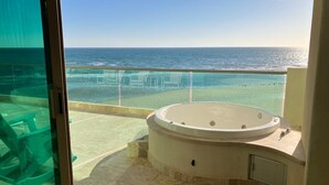 A balcony with a jacuzzi, clear glass doors, and a view of the ocean.