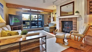 A cozy living room with a fireplace, comfortable seating, and a television displaying a vacation rental sign.