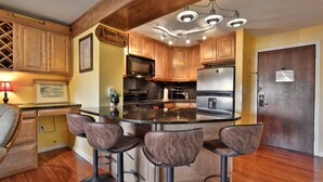 A kitchen with wooden cabinets, a granite countertop, a stainless steel refrigerator, and a bar area with stools.