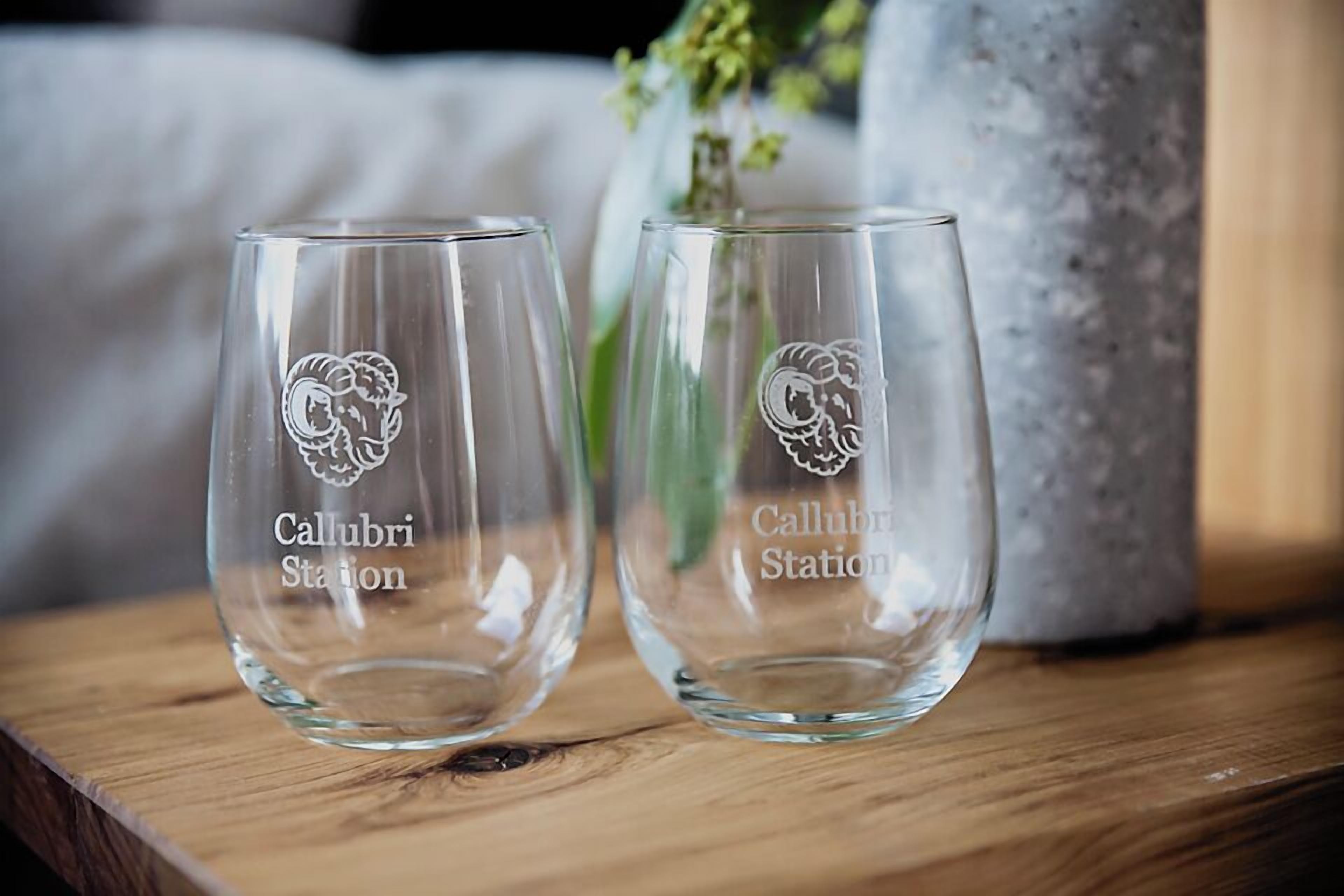 Two empty wine glasses with 'Callibri Station' engraved on them, placed on a wooden surface with a blurred background.