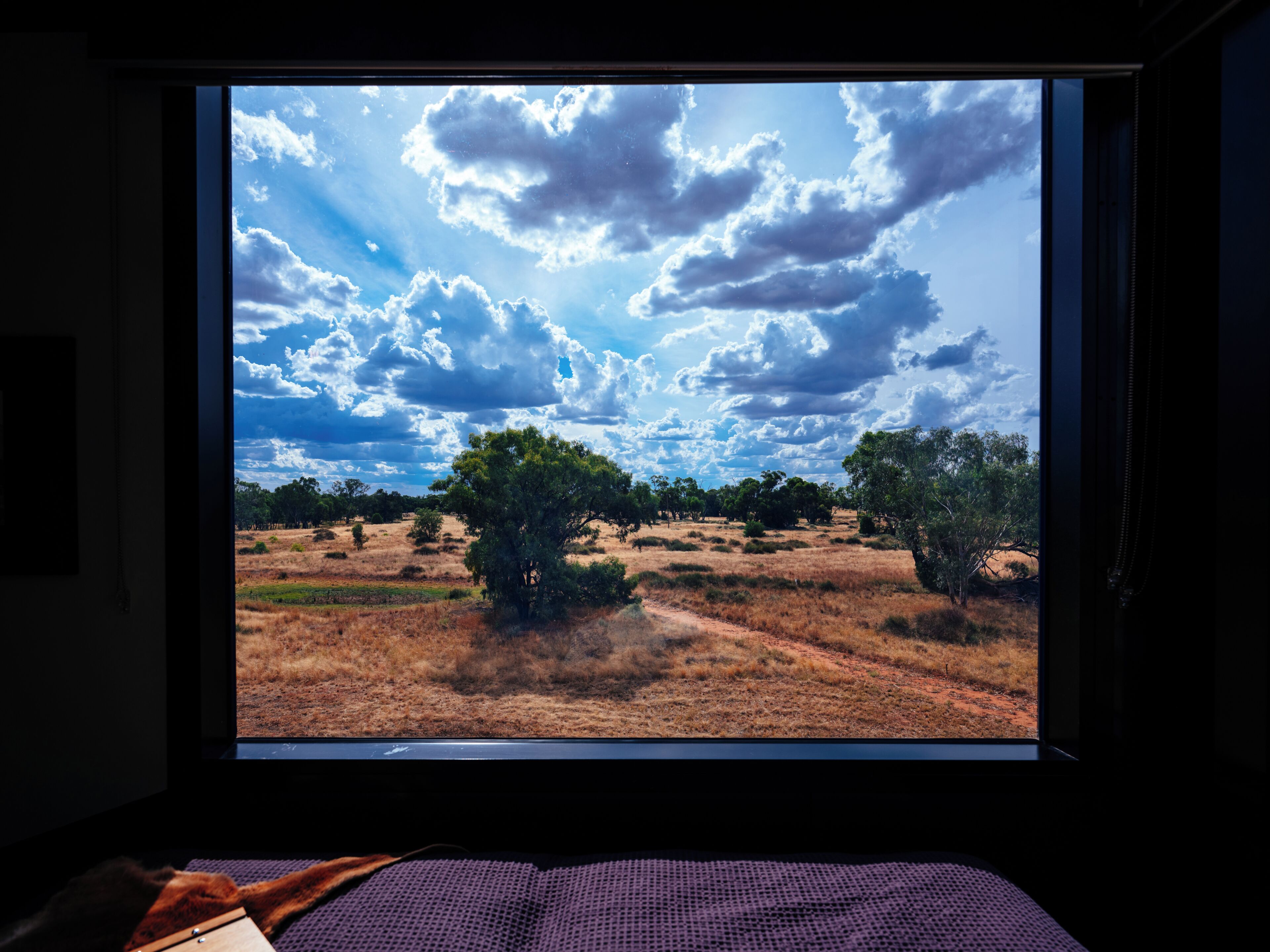 Een kamer met een groot raam, met uitzicht op een landschap met bomen en een heldere lucht.