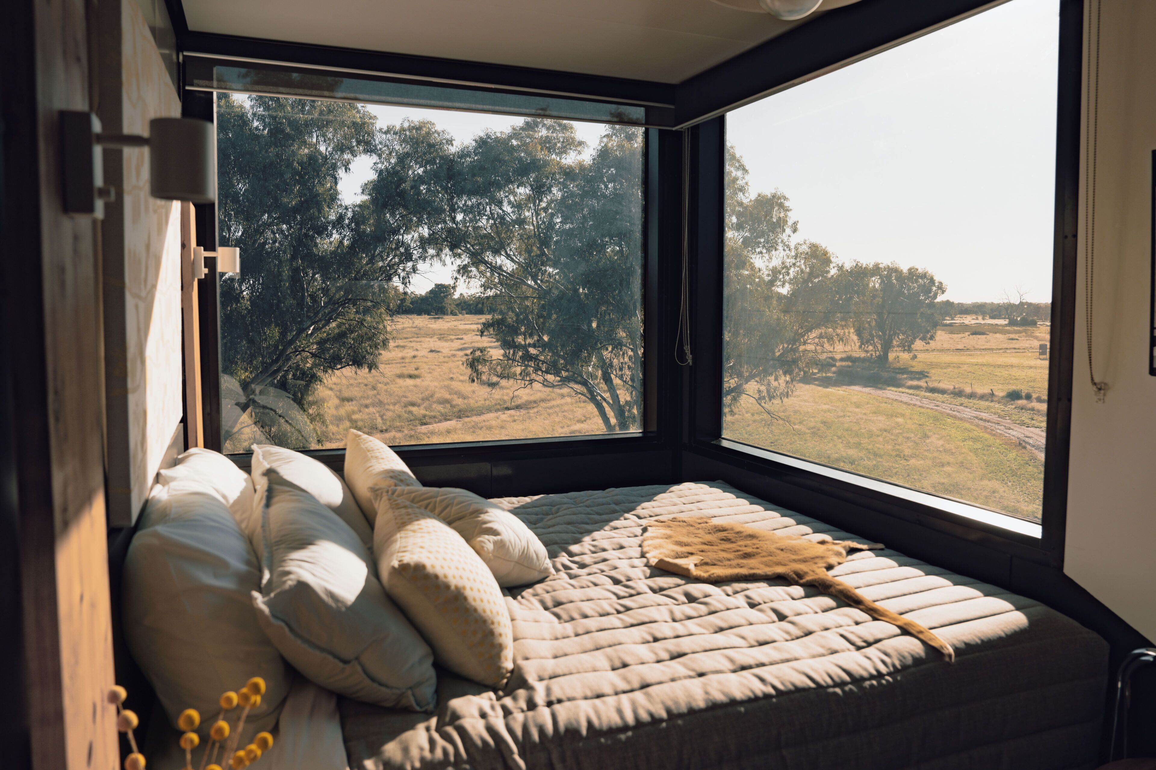 Una cama con vistas a un paisaje rural a través de un ventanal amplio.