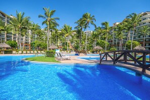 A resort pool with palm trees, lounge chairs, and a wooden bridge. - Cozy Studio with Ocean Views (Nuevo Vallarta)