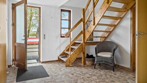 A room with a wooden staircase, a wicker chair, and a stone-tiled floor. - 5 bedroom lovely home in Aakirkeby (Aakirkeby)