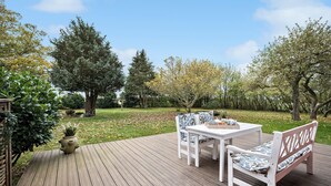 A wooden deck with a white table and chairs, surrounded by trees and a grassy area. - 5 bedroom lovely home in Aakirkeby (Aakirkeby)