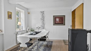 A dining area with a white table, black chairs, a patterned rug, a tall plant, and a painting on the wall. - 5 bedroom lovely home in Aakirkeby (Aakirkeby)