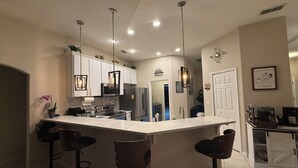 Una cocina moderna con una isla grande, taburetes de bar, luces colgantes y un refrigerador.