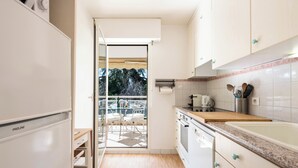 A modern kitchen with white cabinets, a wooden countertop, and a view of the outdoors through a glass door. - A-Br – Quiet, Infinity Pool & Private Parking (Cannes)