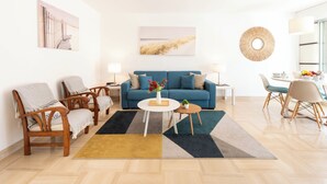 A modern living room with a blue sofa, wooden chairs, a coffee table, and a dining area with a white table and chairs. - A-Br – Quiet, Infinity Pool & Private Parking (Cannes)