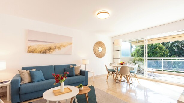 A modern living room with a blue sofa, a coffee table, and a dining area with chairs and a table. - A-Br – Quiet, Infinity Pool & Private Parking (Cannes)