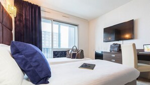 Ein Hotelzimmer mit Bett, Schreibtisch, Stuhl, Fernseher und einem Fenster mit Vorhängen.