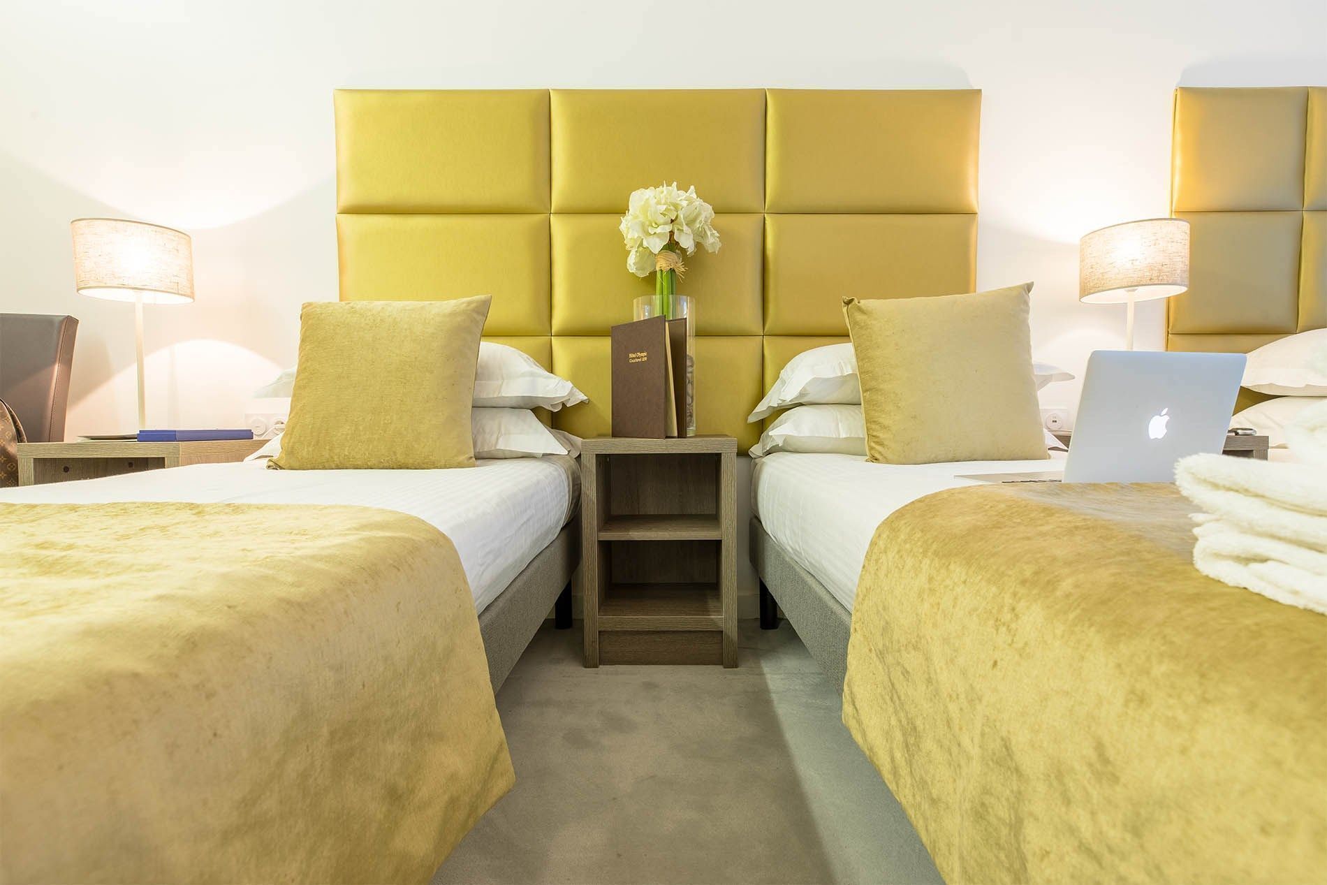 Une chambre d’hôtel avec deux lits, une table de chevet, un ordinateur portable et un vase avec des fleurs.