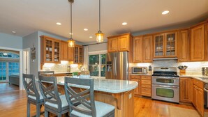 Una cocina moderna con armarios de madera, electrodomésticos de acero inoxidable y una isla central con taburetes de bar.