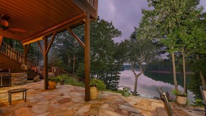 Un patio de piedra con una pérgola de madera, mobiliario exterior y vistas a un lago.