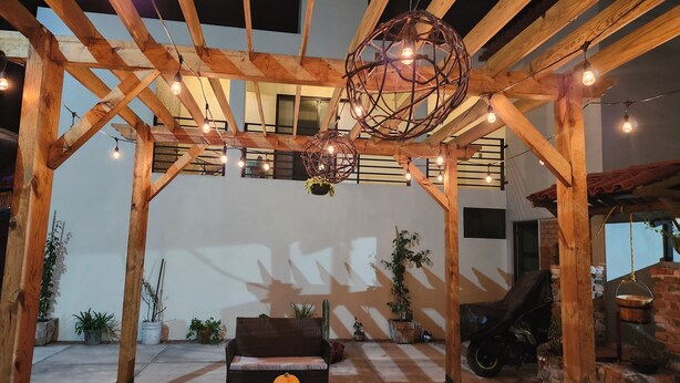 Un espace extérieur abrité, doté de poutres en bois, de luminaires suspendus et de plantes en pot.
