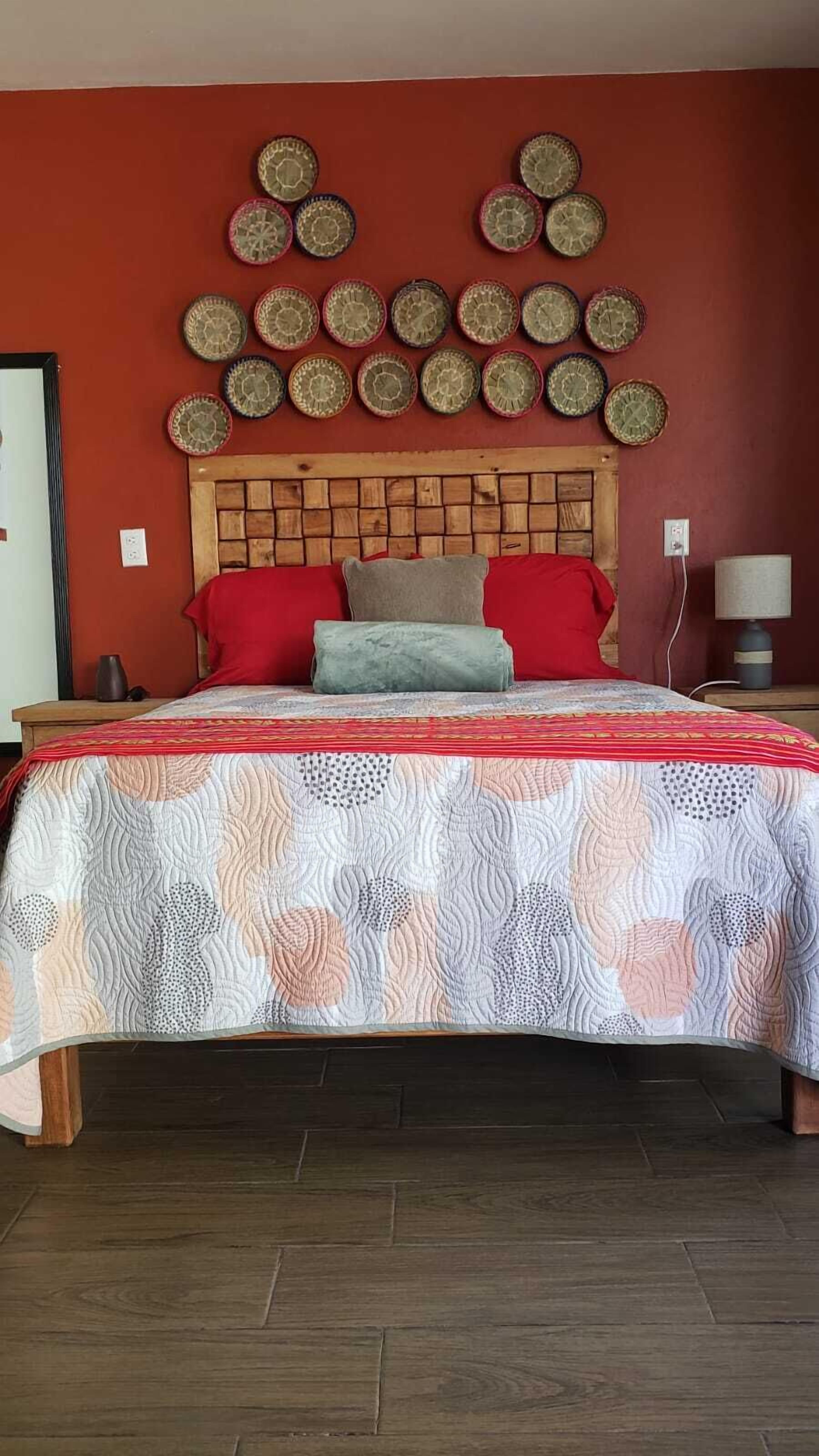 A bedroom with a wooden headboard, a patterned bedspread, and a wall decorated with circular woven items.