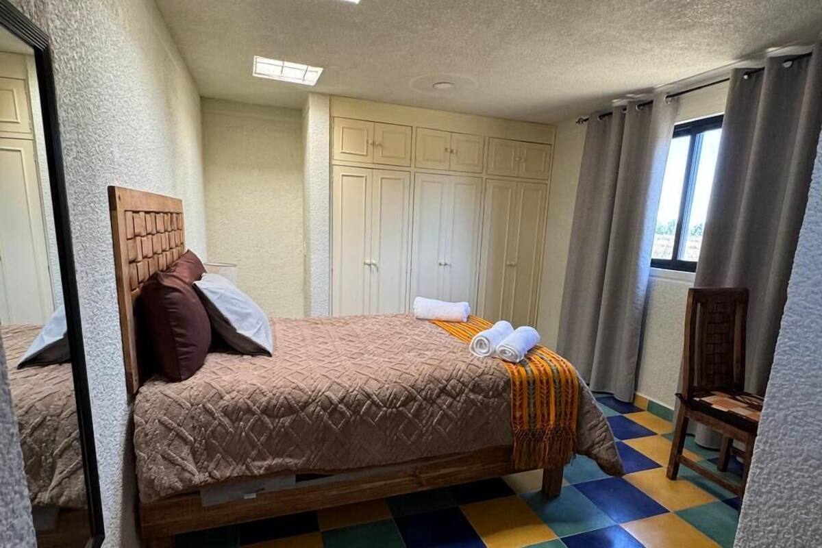 A bedroom with a bed, a mirror, a wardrobe, a chair, and a window with curtains.