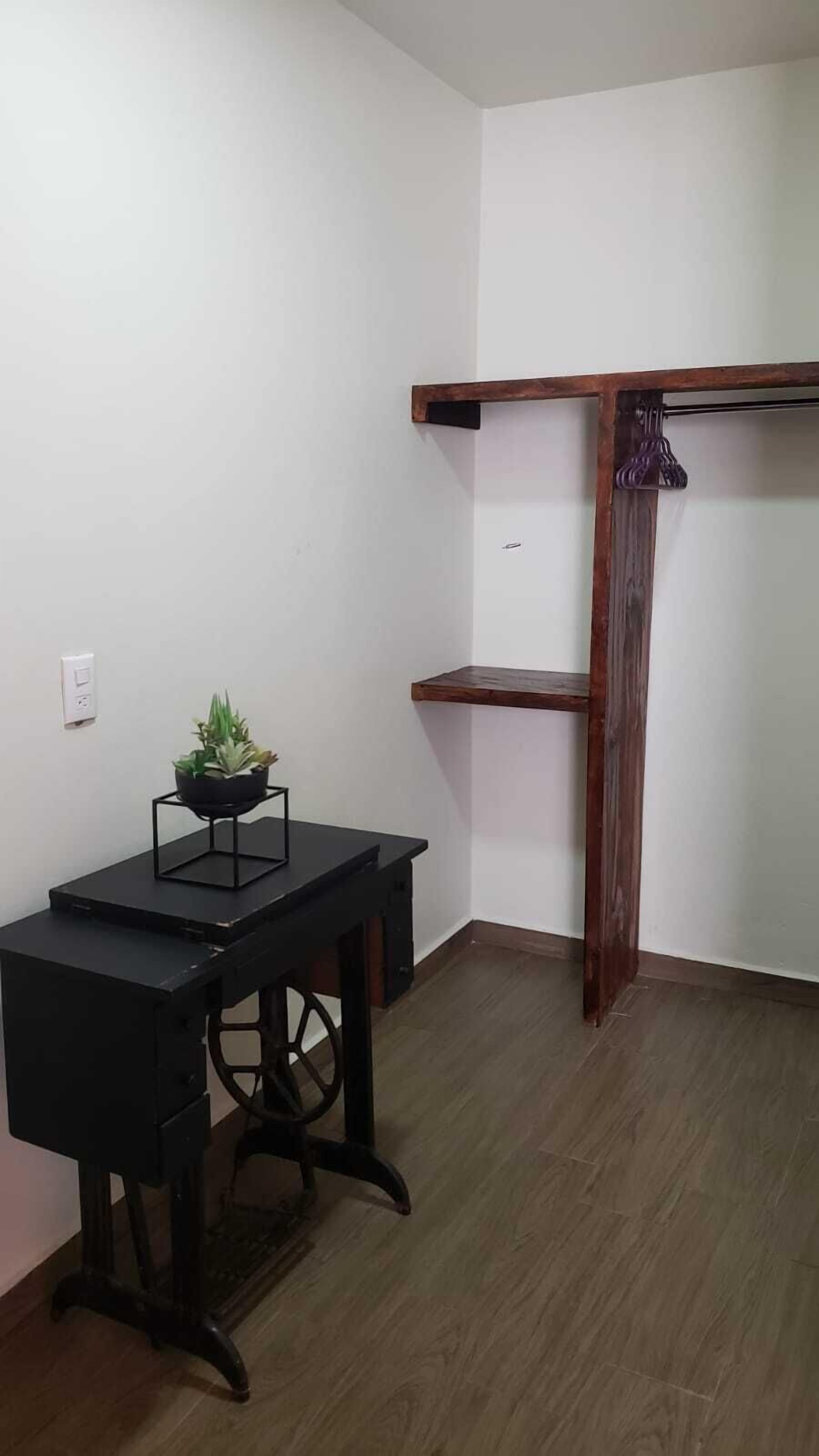 A corner room with a wooden desk, a small potted plant, and a wooden coat rack.