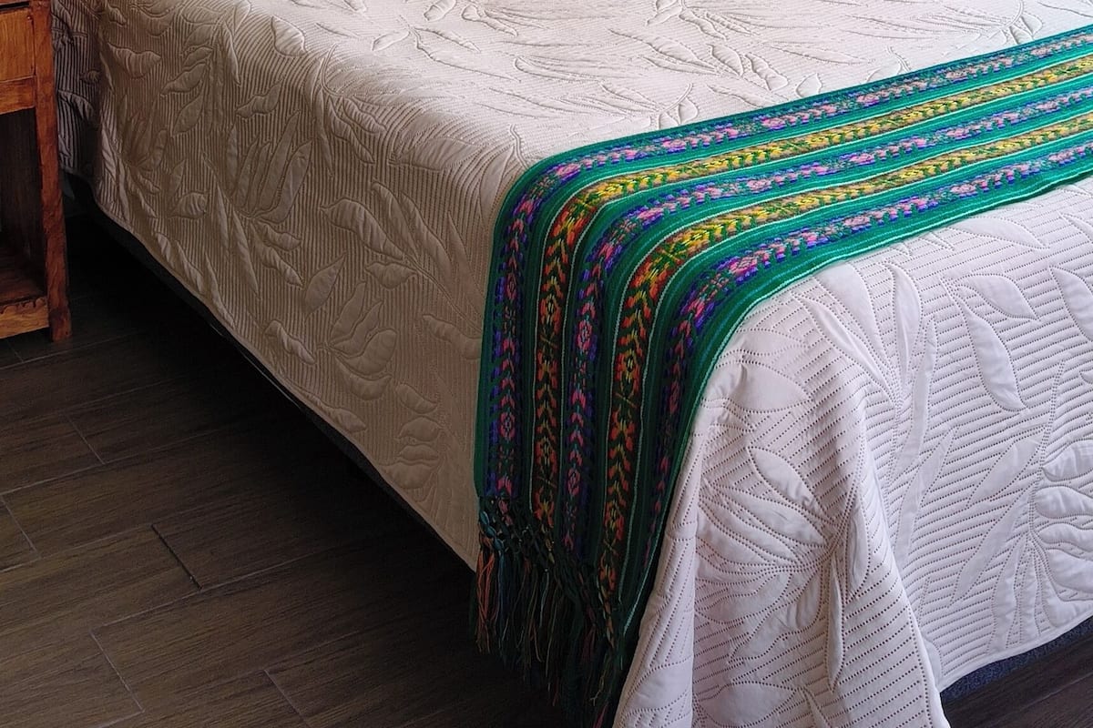 A neatly made bed with a patterned quilt, a wooden headboard, and a colorful artwork on the wall.