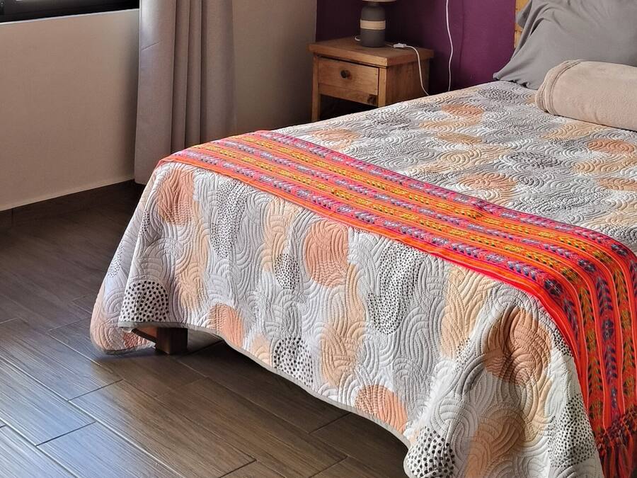 Un dormitorio con cama, ventilador de techo, mesita de noche, ventana con cortinas y vistas al exterior.