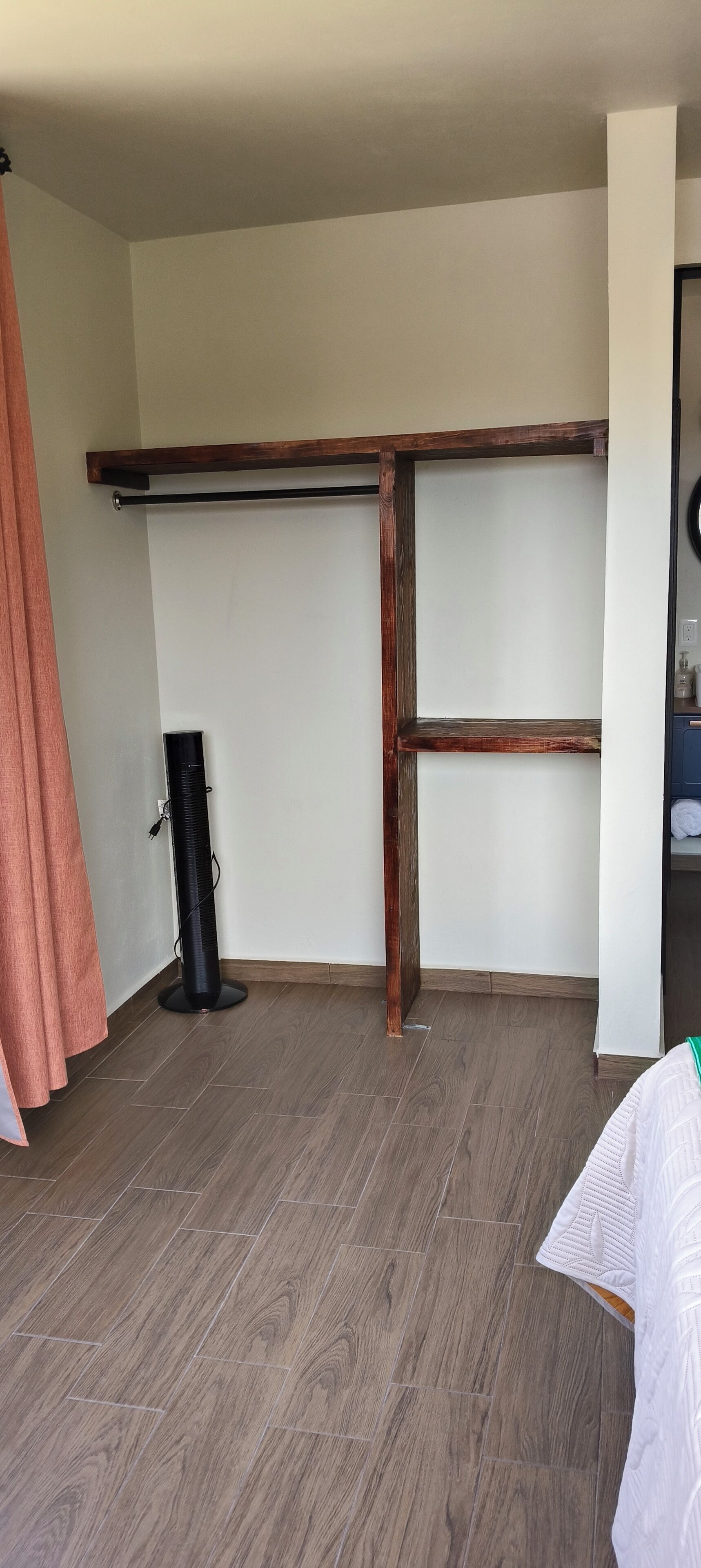 A room with a wooden floor, a standing fan, and a wooden beam structure.
