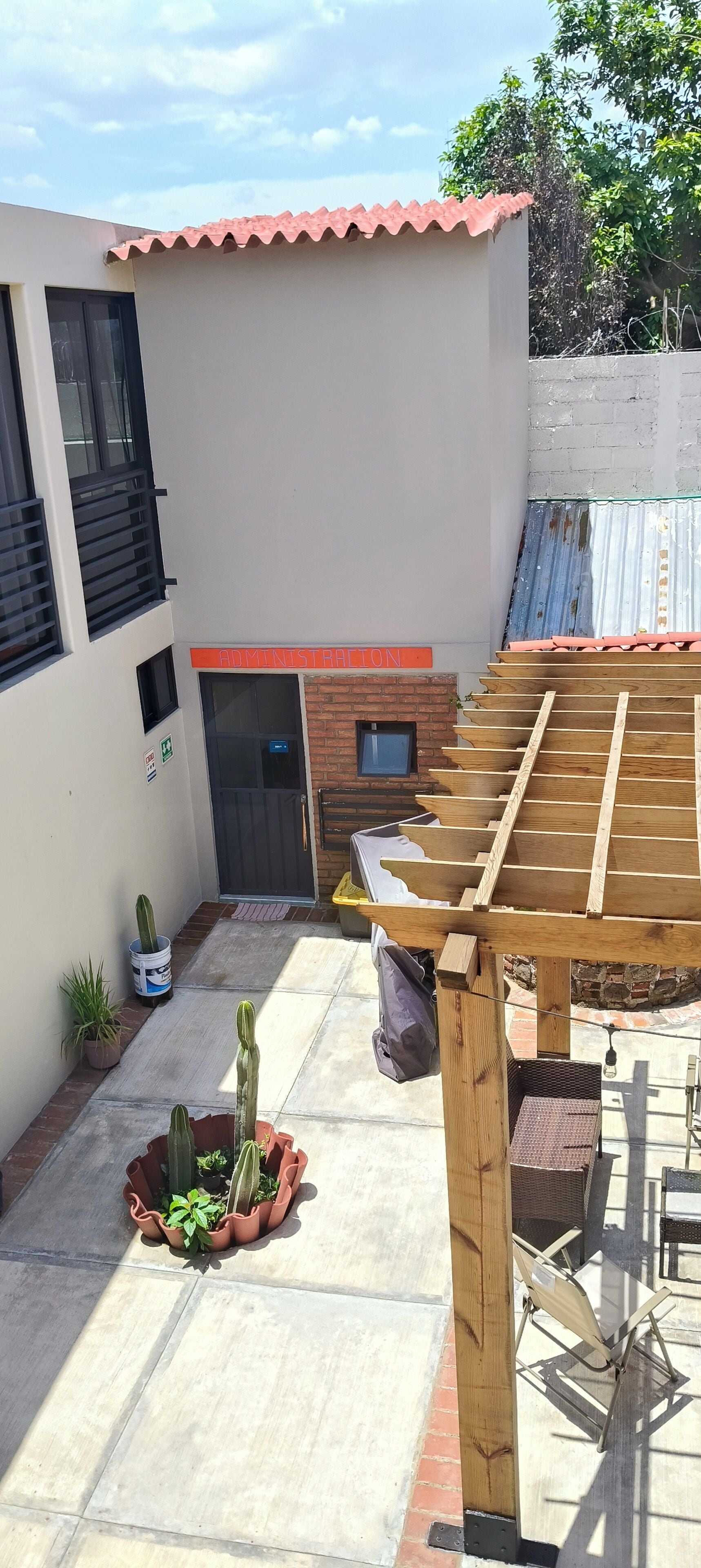 A courtyard with a wooden pergola, a brick wall, a metal gate, and potted plants.