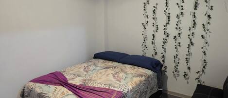A bedroom with a bed, a TV mounted on the wall, and a hanging plant.
