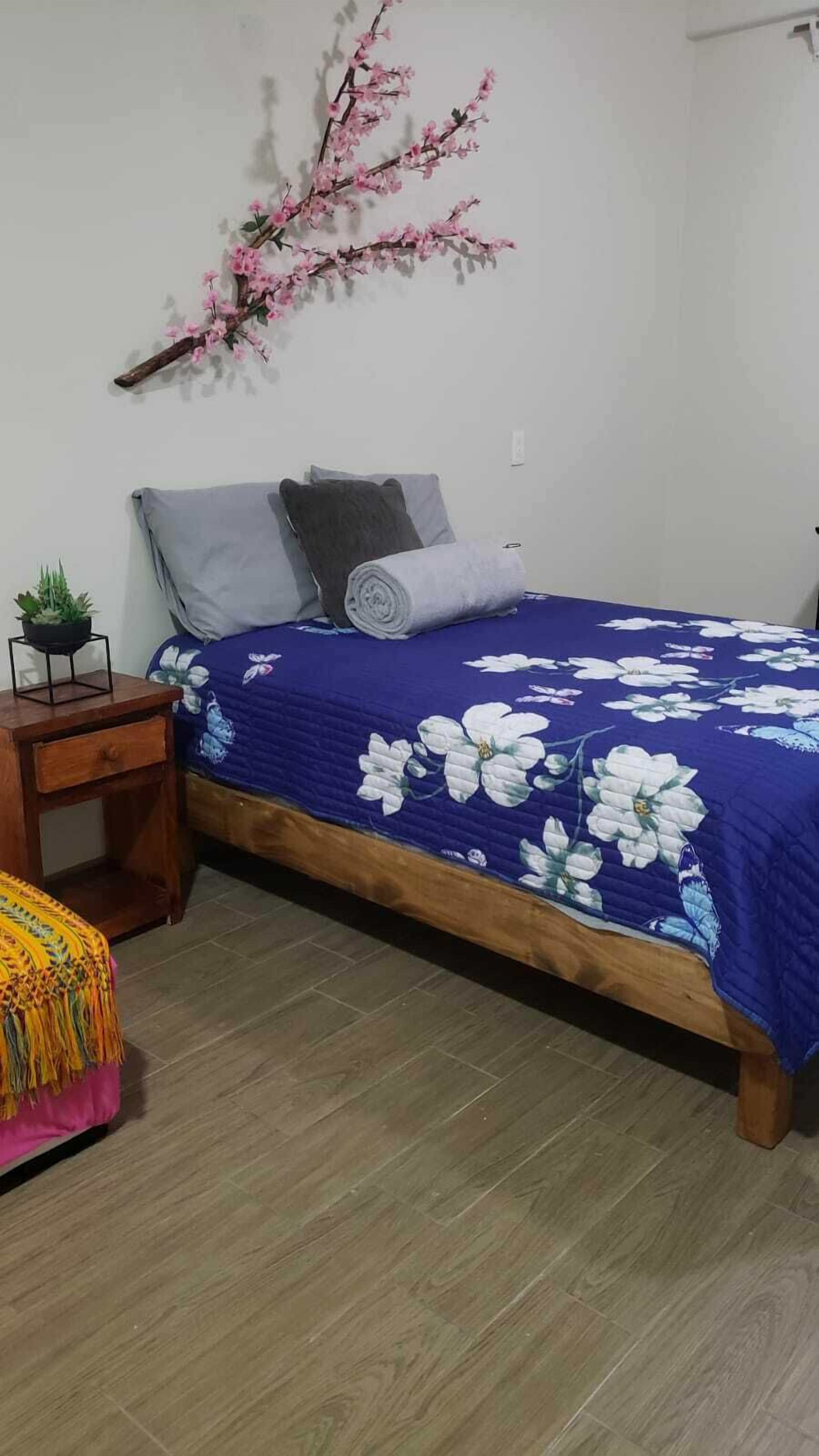 Un dormitorio con cama, mesita de noche, silla y planta en la pared.
