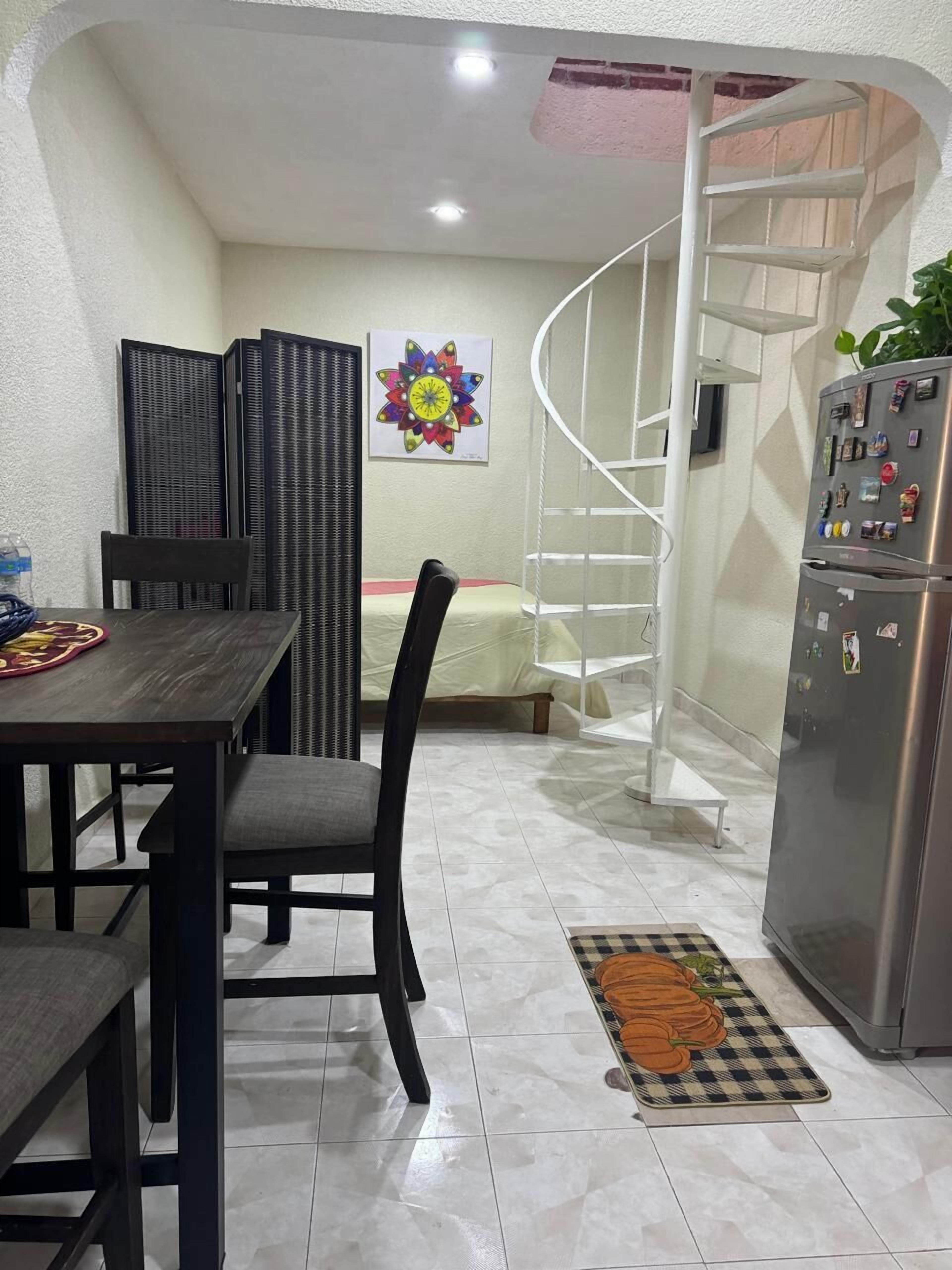 A compact kitchen with a dining area, a spiral staircase, and a refrigerator with magnets.