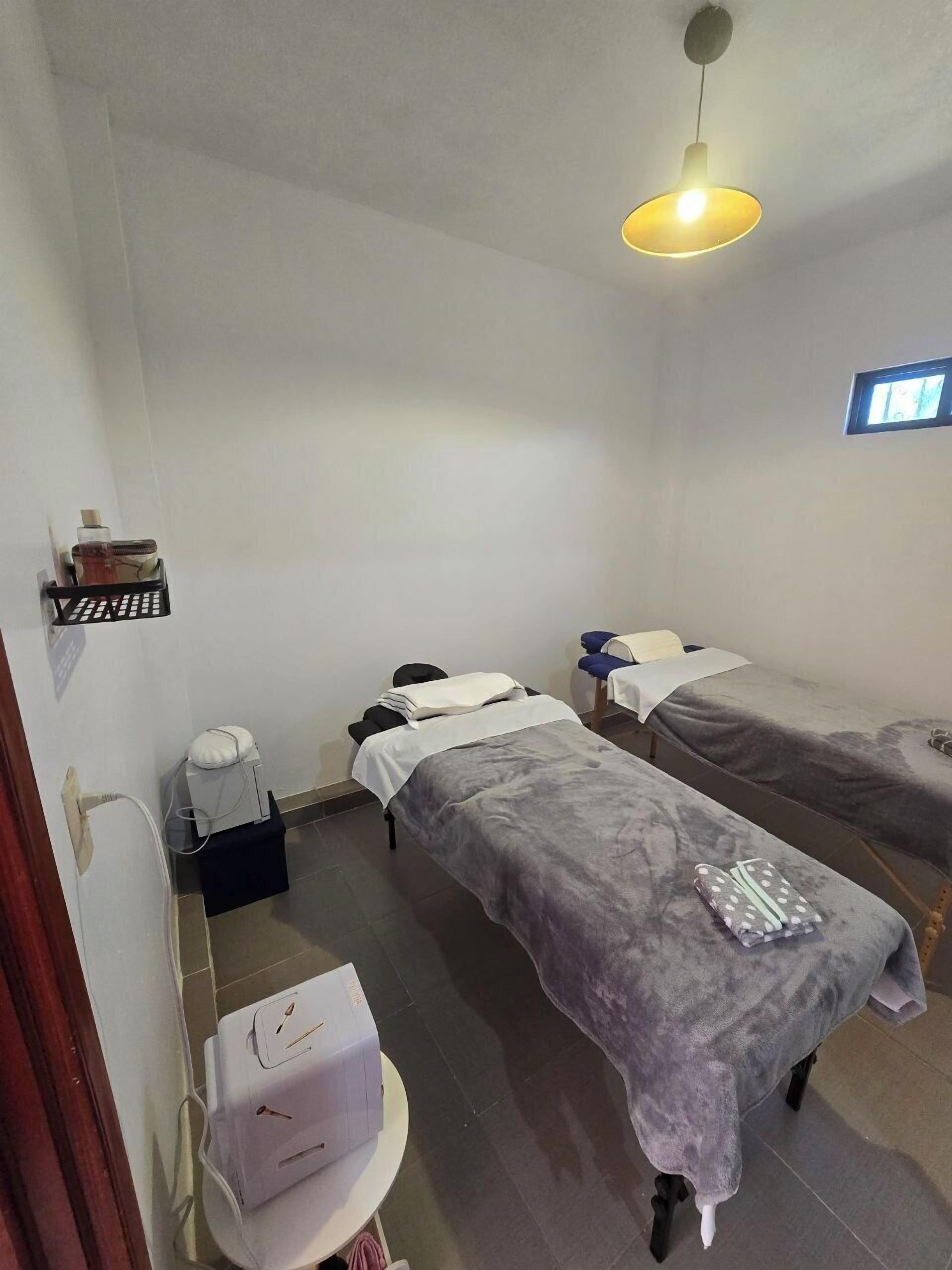 A room with two beds, a small shelf with toiletries, a desk with a computer, and a window.