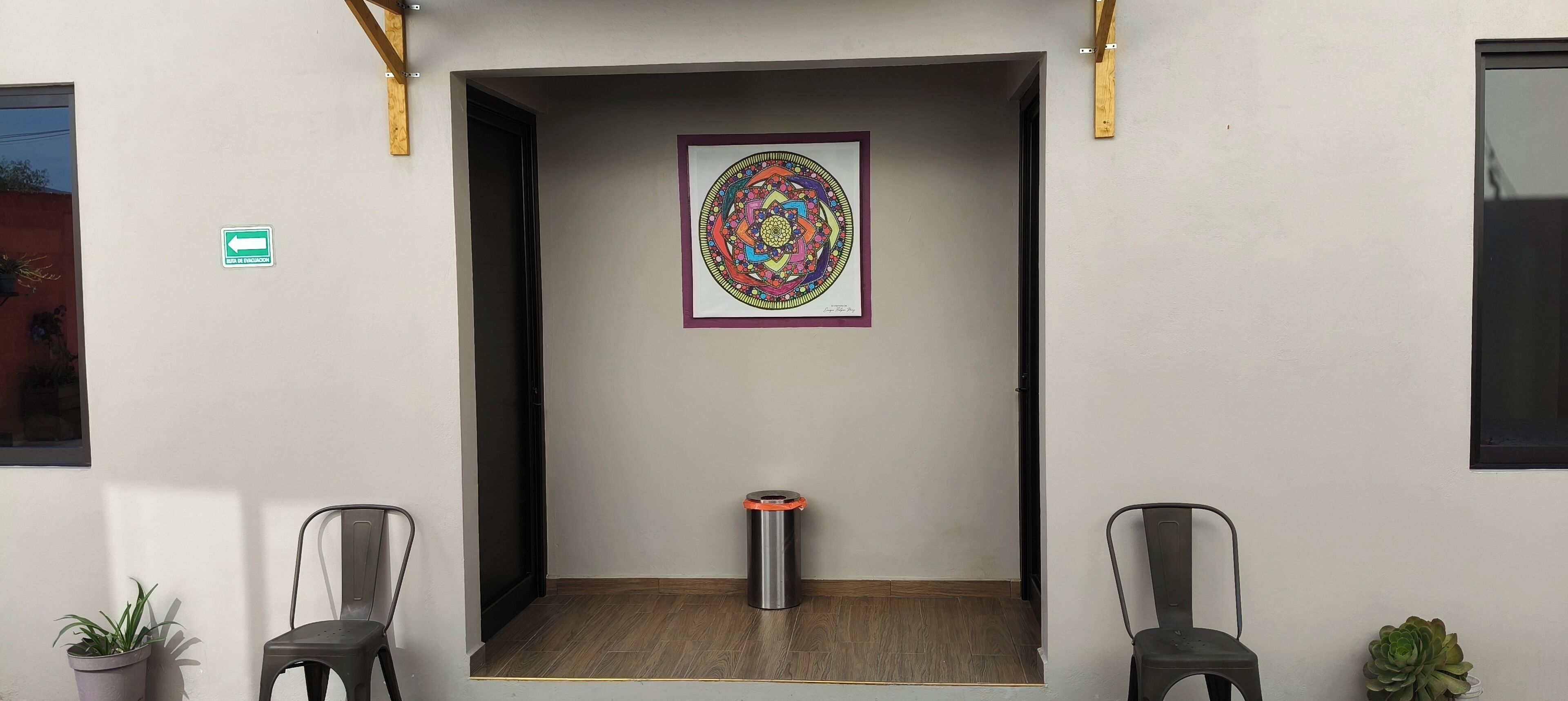 En hall med ett inramat konstverk på väggen, en papperskorg och två stolar.